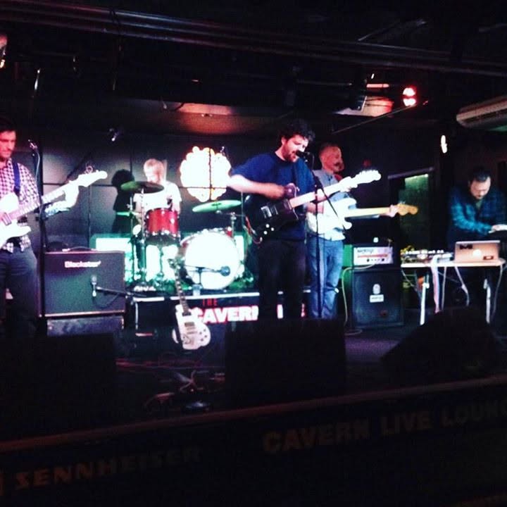 The band on stage at the Cavern Live Lounge in Liverpool, a Sennheiser banner along the front of the stage